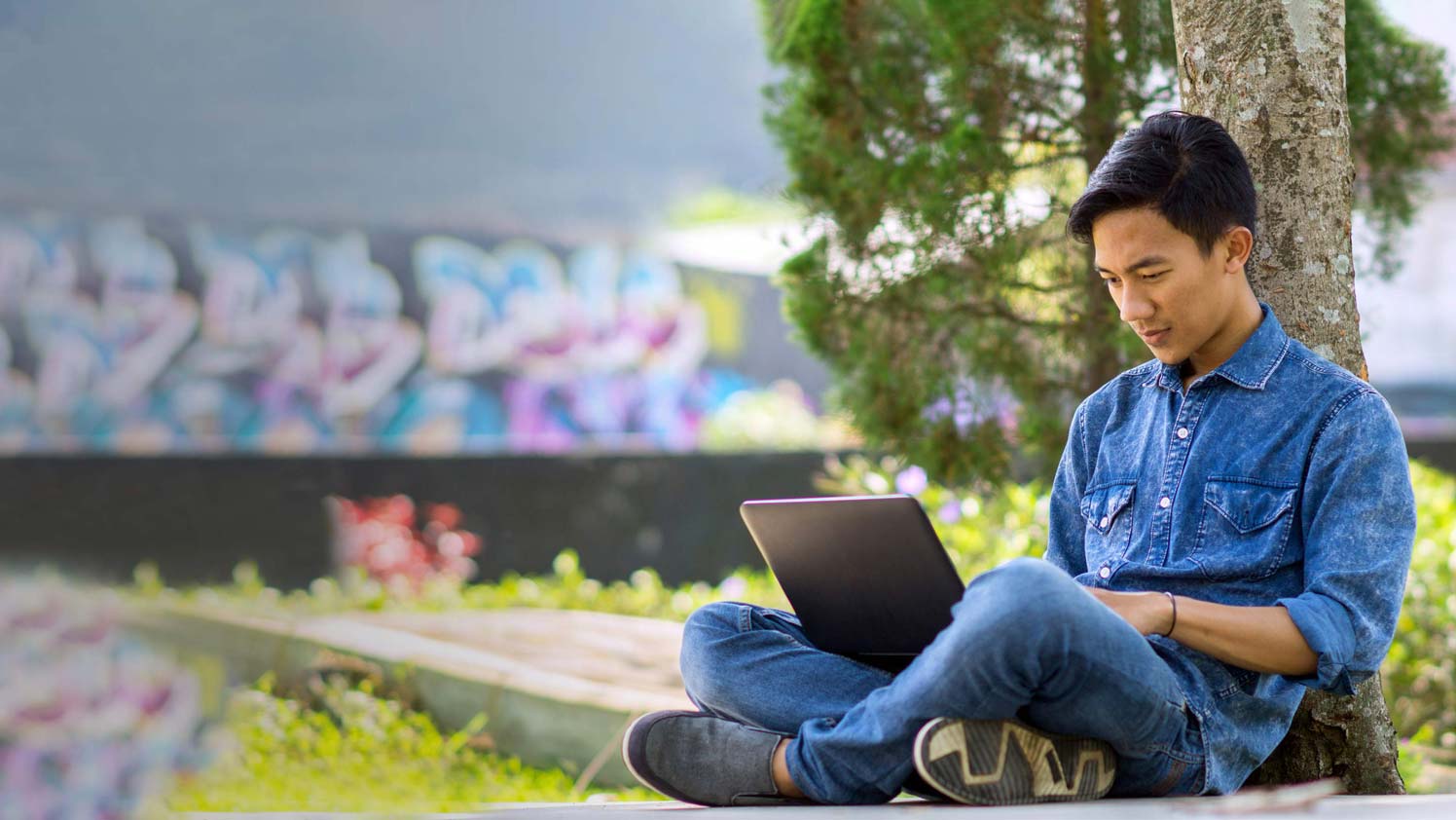 Man sitting down against a tree using laptop