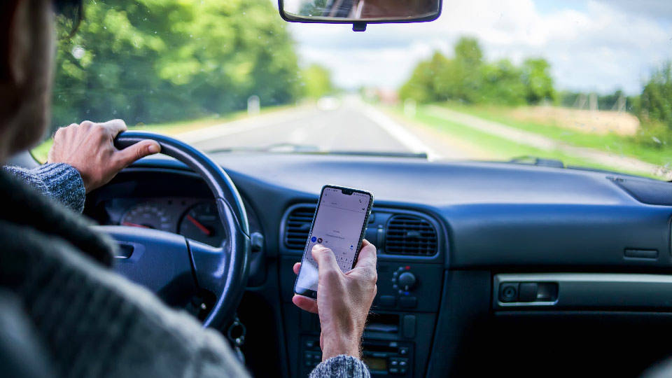 Bild eines Autofahrers, der abgelenkt ist, weil er auf einen Smartphone-Bildschirm schaut.