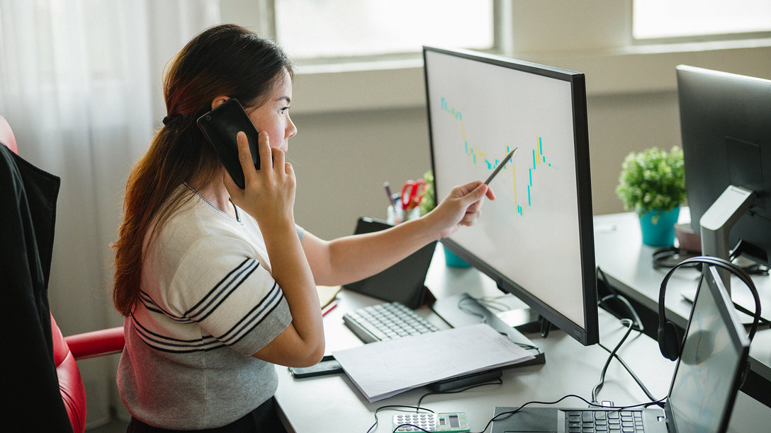 Foto de una mujer hablando por teléfono frente una computadora.