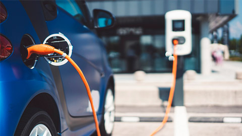 A blue electric vehicle charging with an orange cord