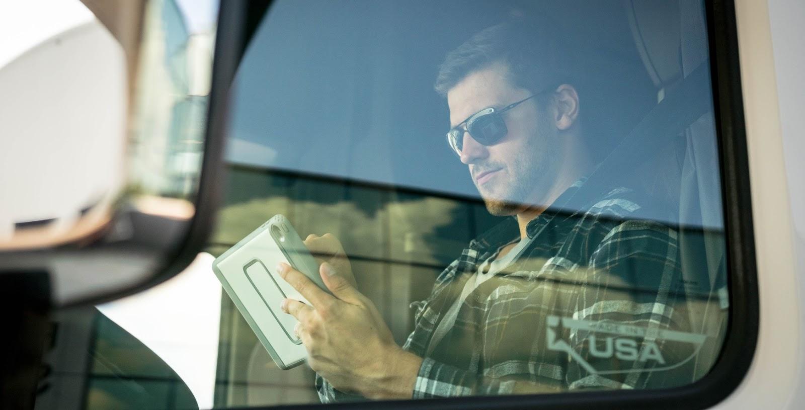 Man sitting in truck and holding a tablet to complete HOS logging requirements.