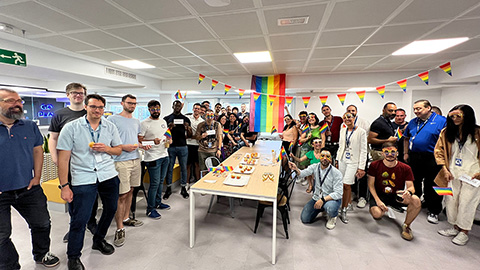 Menschen stehen um einen Tisch mit Regenbogenflaggen und feiern den Pride Month.