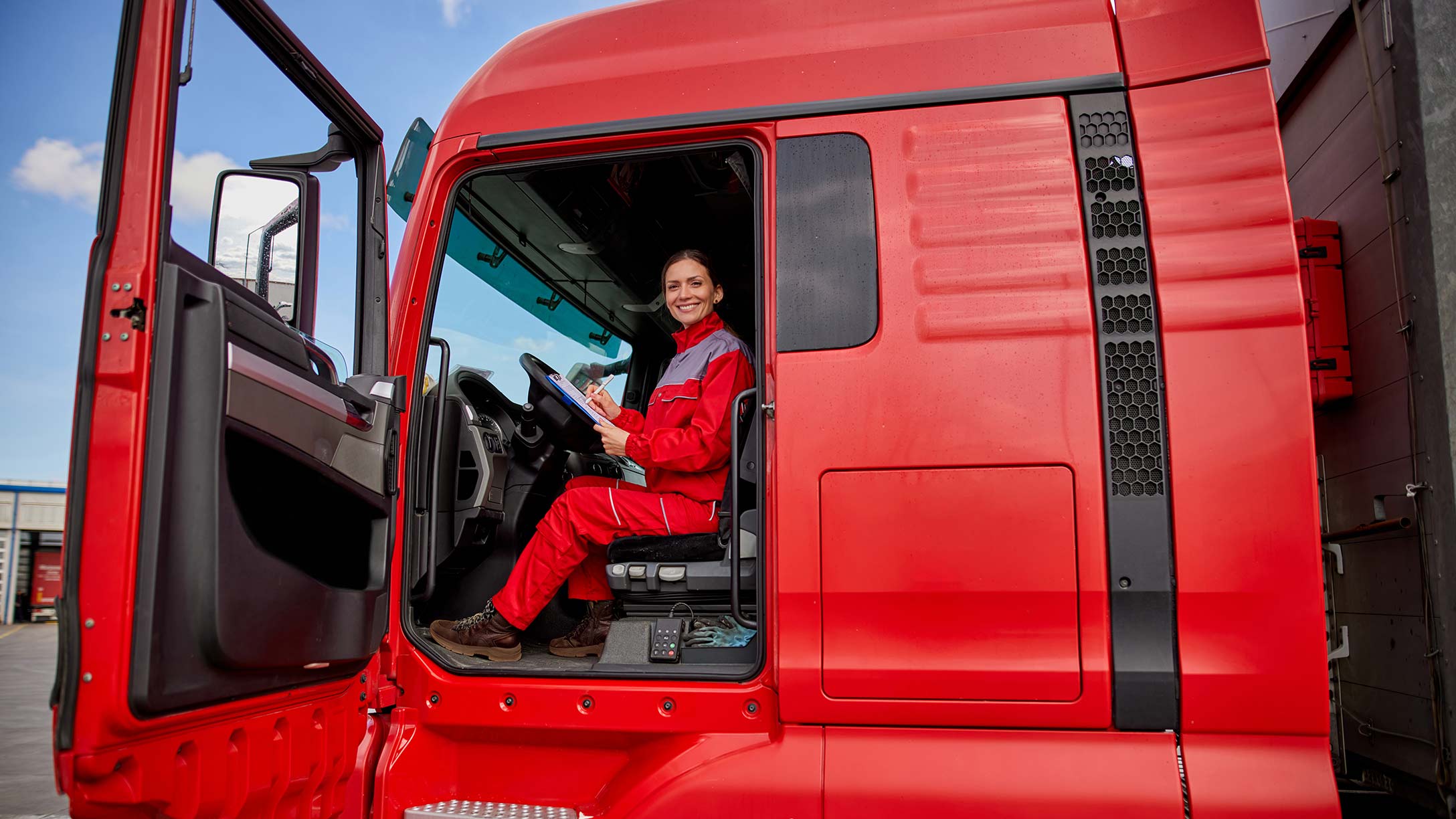 A woman driver sitting in the driver seat in a red truck with a writing pad in her hand 