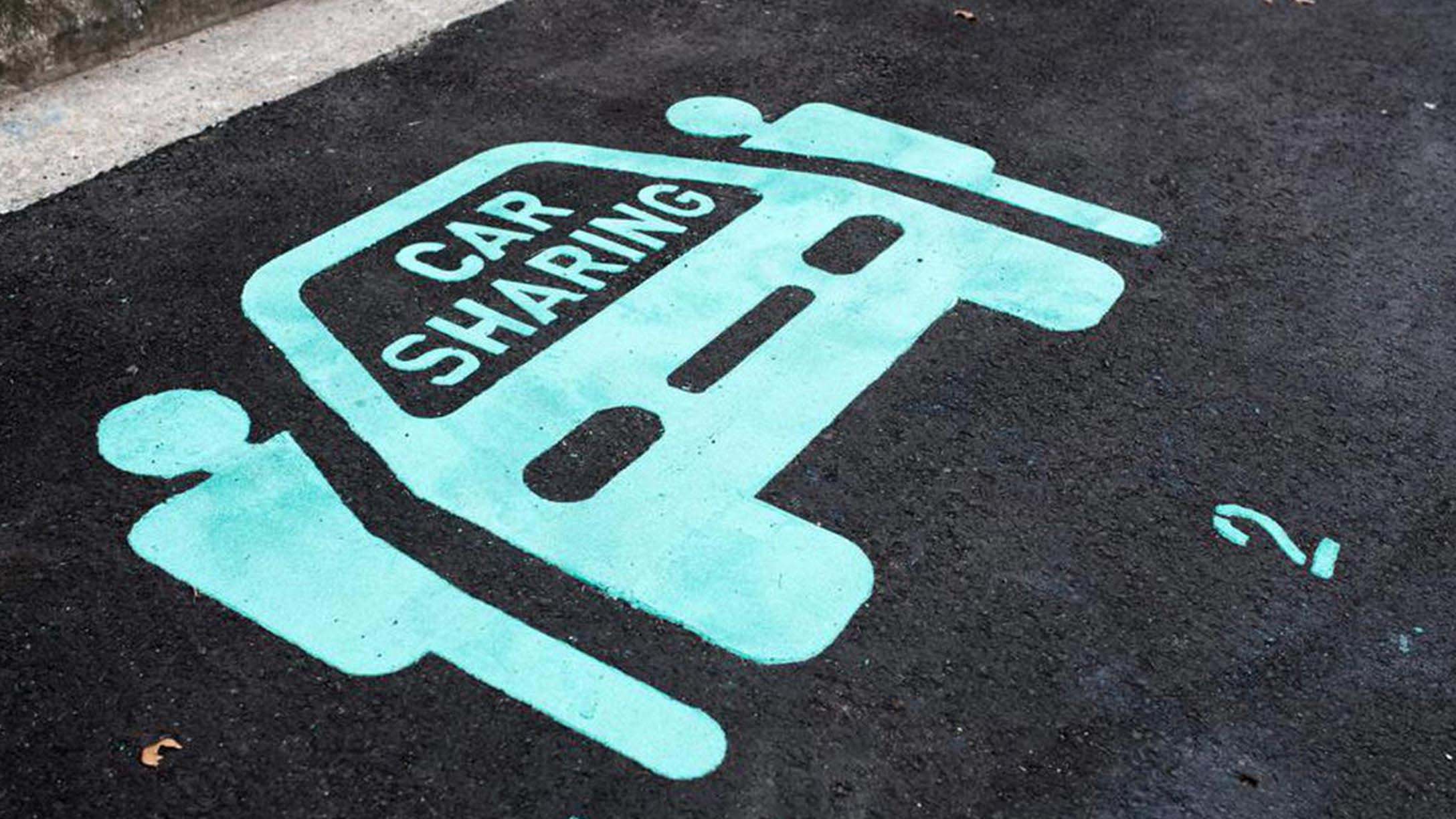 Chalk drawing on road of two people next to a car with the text 'Car Sharing'
