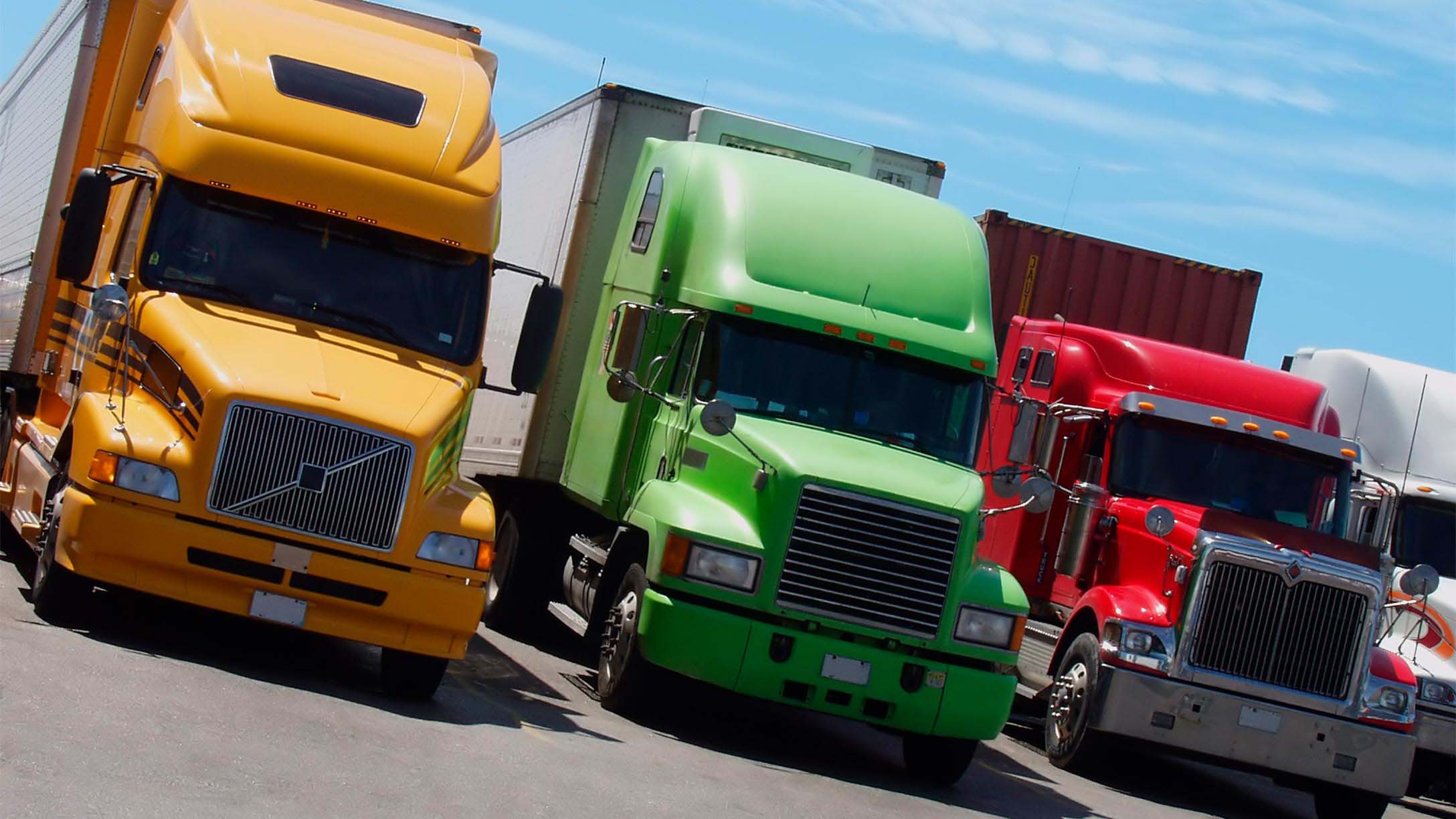 Three semi trucks lined up, one is yellow, one is green and one is red