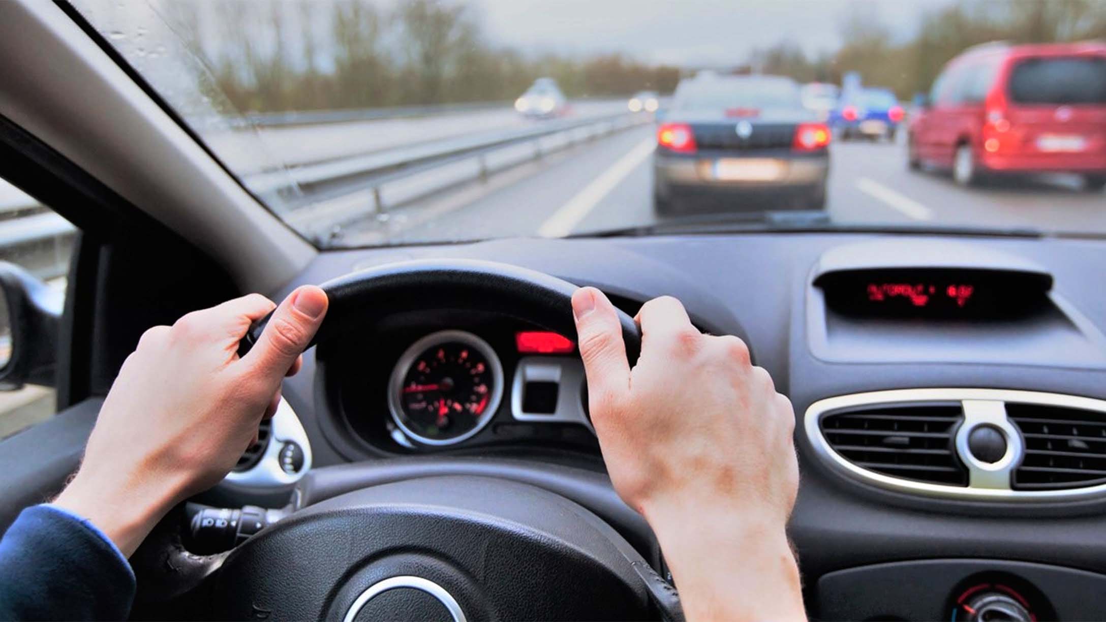 Point of view of a person driving with two hands on the steering wheel on a highway