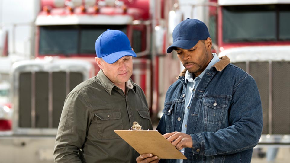 Two people looking at clipboard in front of two trucks