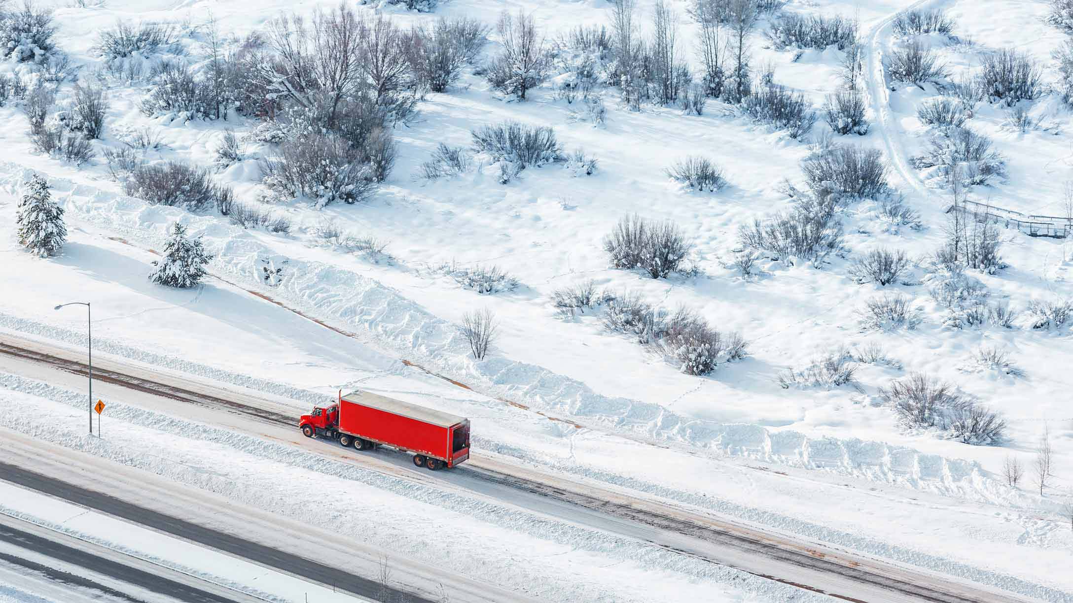 Transport truck driving on road surrounded by trees covered in snow