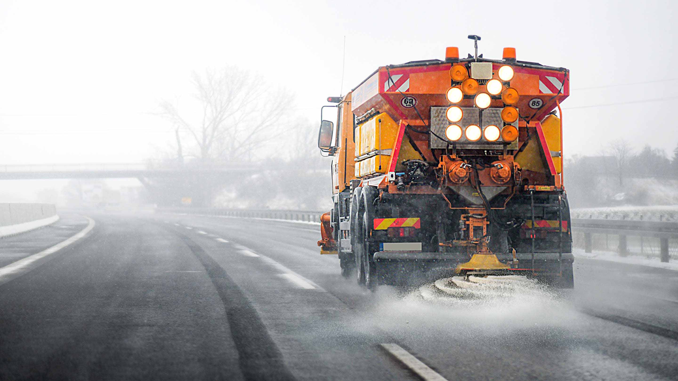 Ein Winterdienstwagen fährt eine Straße entlang und streut Salz.
