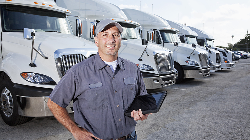 Smiling man wearing a cap and work wear standing on front of parked trucks