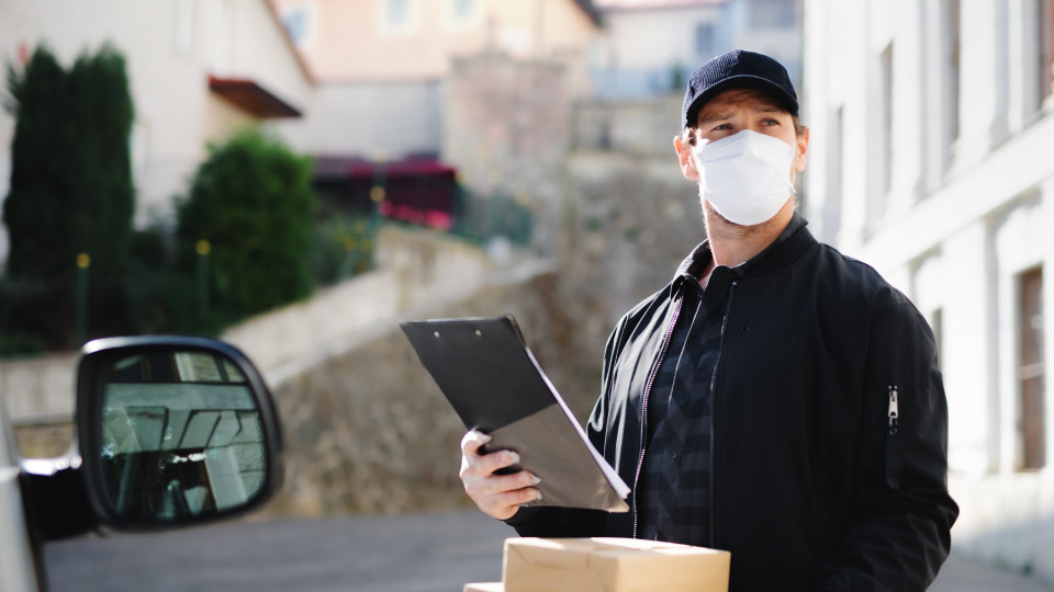Foto de um reparador com sua pastilha eletrônica e um pacote na mão, em pé em um dia ensolarado em frente ao furgão de entrega.