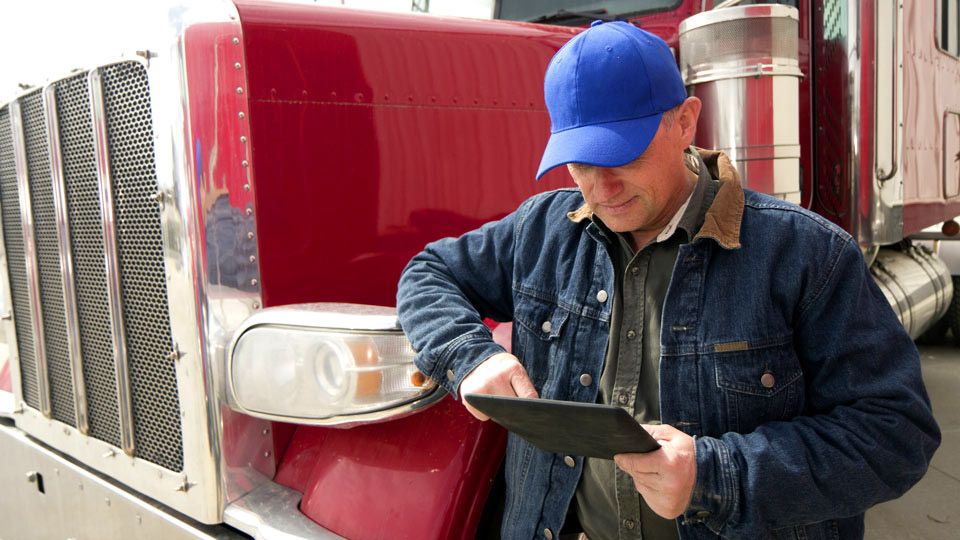 Foto de un hombre usando un tablet delante de un camión pesado rojo. 