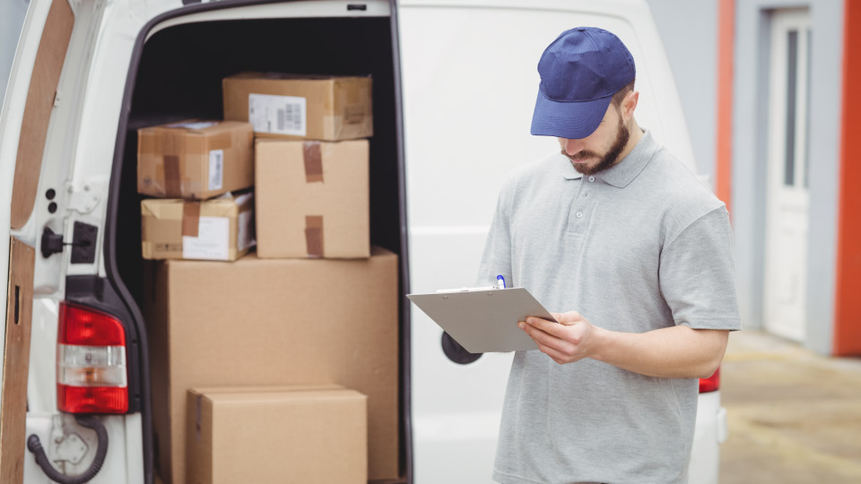 Foto de un hombre con un tablet en la mano en frente de un camión de última milla con paquetes dentro.