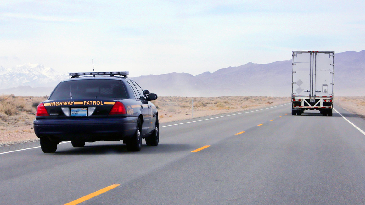 Highway patrol car pulling over a semi truck in the desert