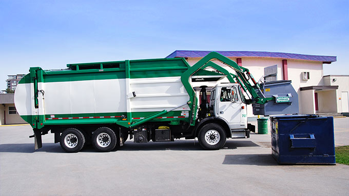 Green and white garbage truck lifting a blue dumpster