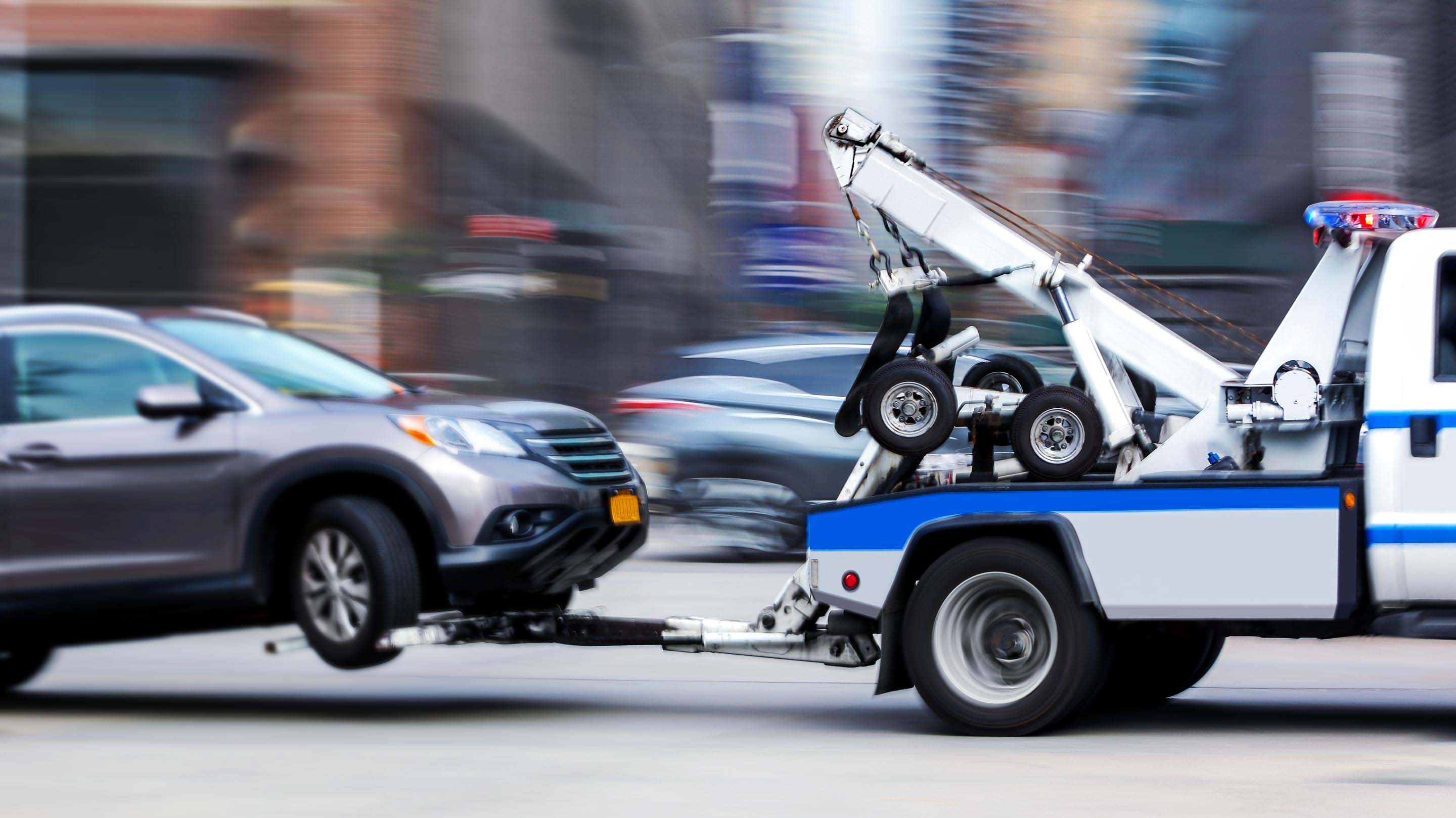 Grey SUV being towed on a busy street by a blue and white tow truck