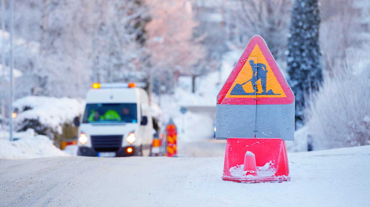 Vehicles stopped on a snowy road with a road work pylon in the foreground