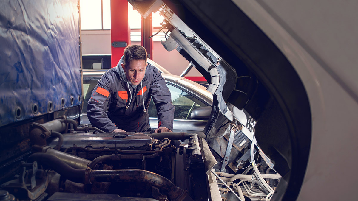 Male mechanic looking at the engine of a semi truck, performing maintenance