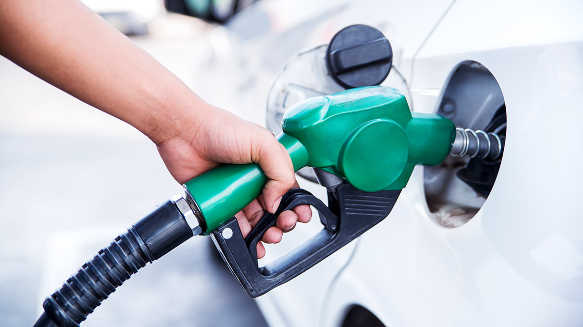 Person using green gas pump to fill white car with gas