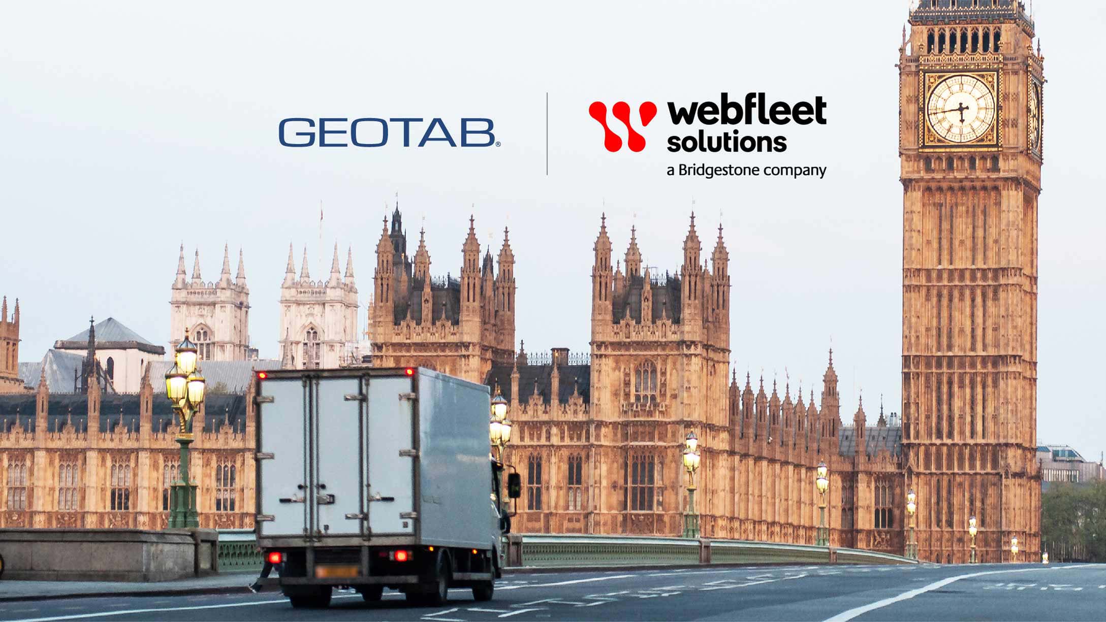 Transport truck driving in front of tall buildings in London, U.K. with Geotab and Webfleet Solutions logo in background