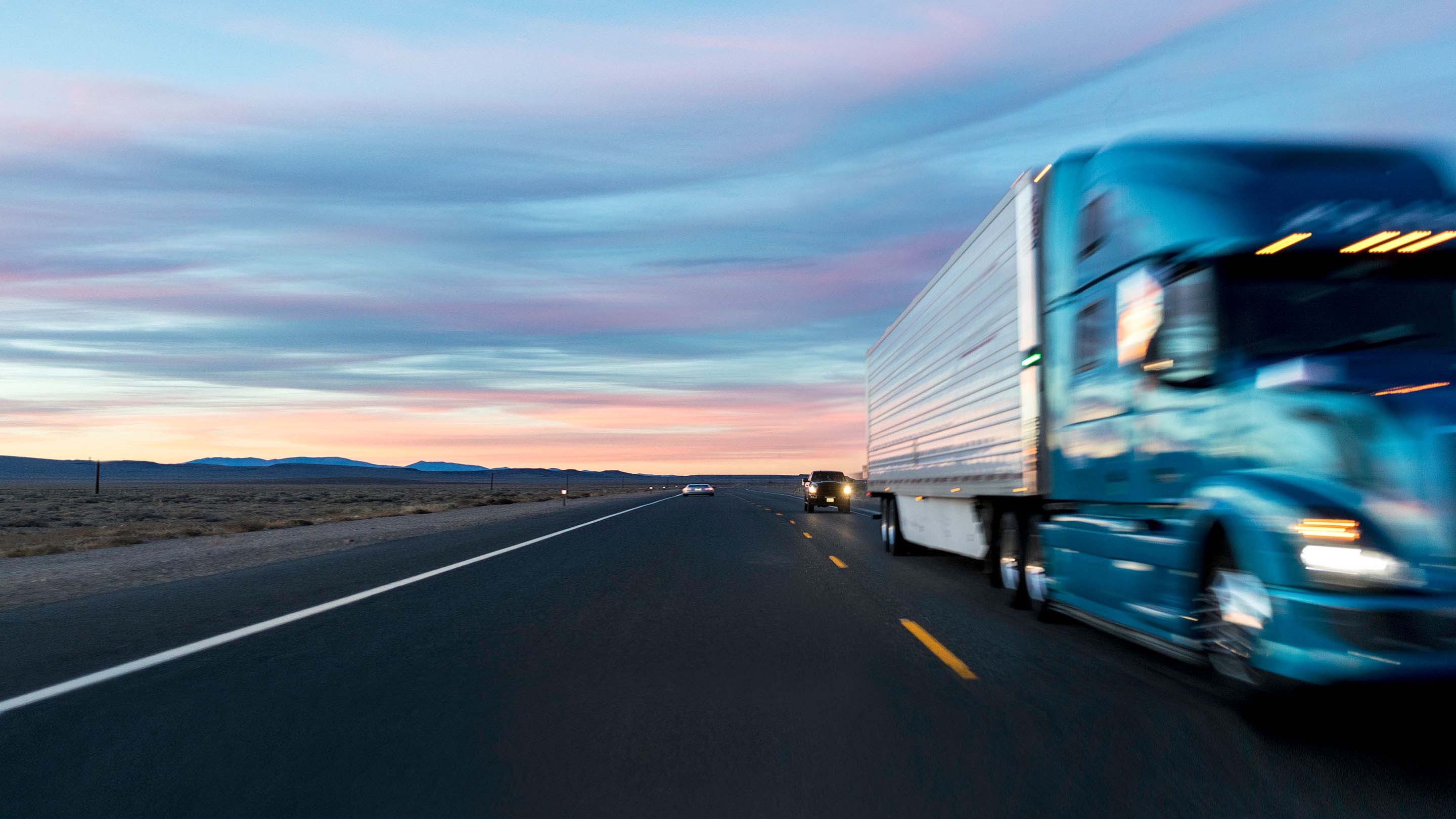 Blue truck driving on road with sunset in the background