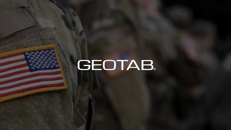 Close up an American flag patch on the arm of an American solider with a dark navy overlay and the Geotab logo.