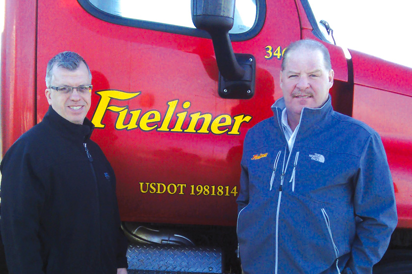 Two men standing in front of a red Fueliner truck