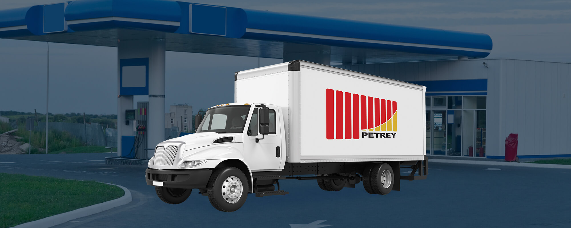 White delivery box truck with PETREY's company logo on it and blue gas station in the background.