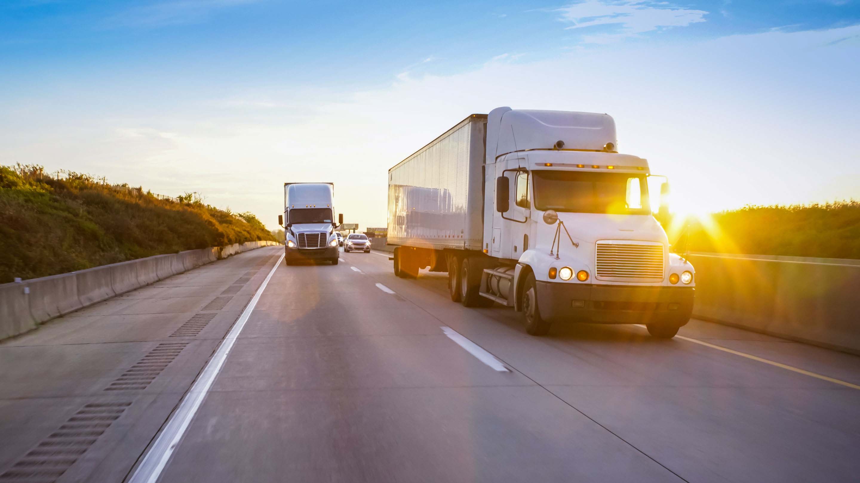Trucks and cars driving on a road with a sunset in the background