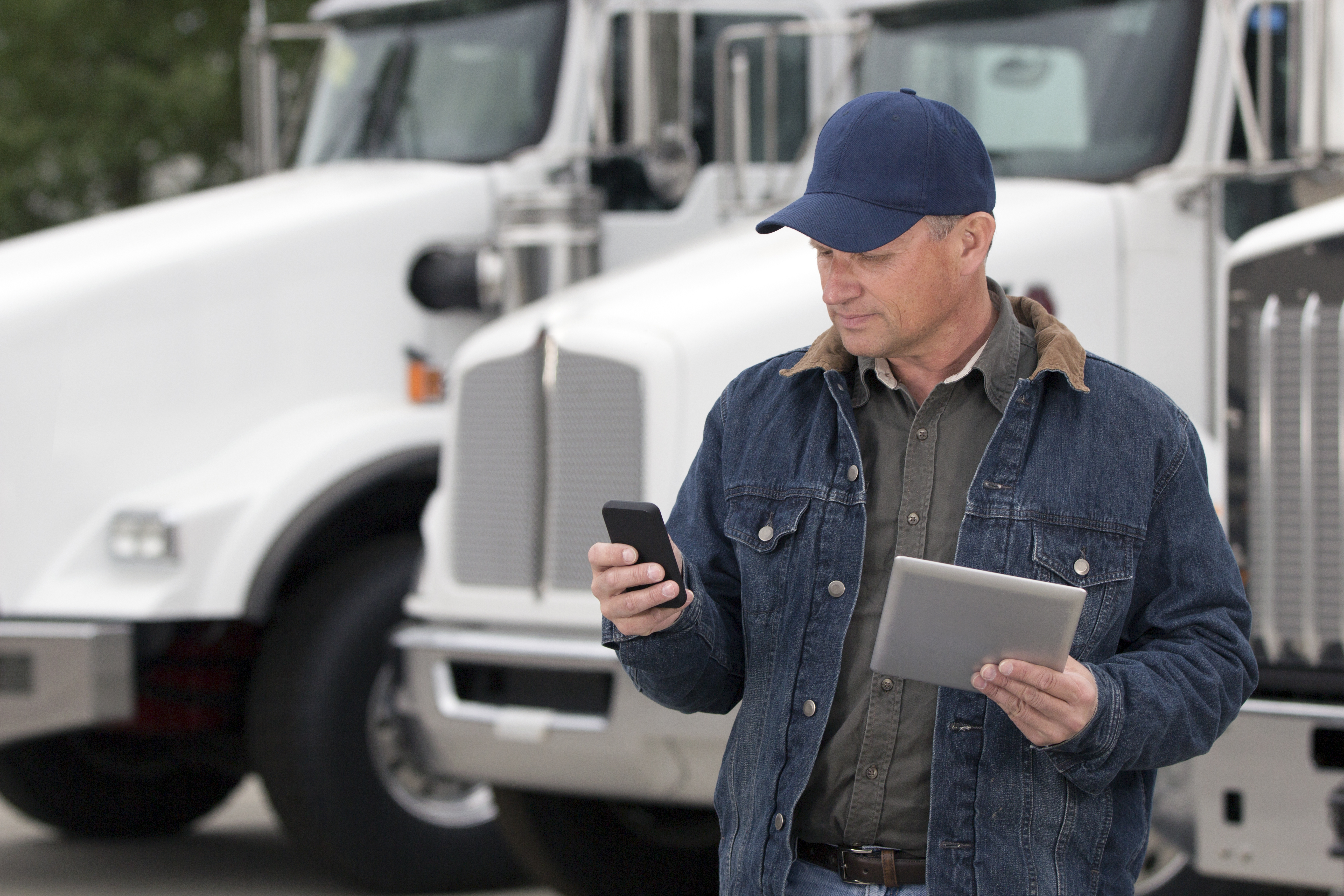 Fleet manager checking telematics data on a phone and tablet beside trucks