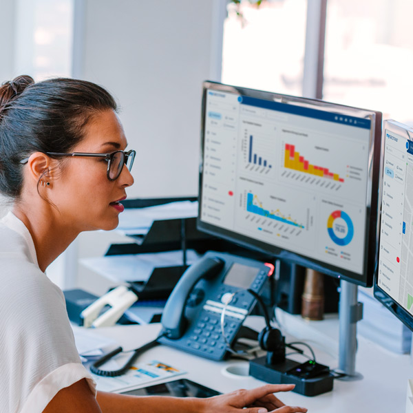 Woman sitting at a desk with two monitors displaying MyGeotab dashboard