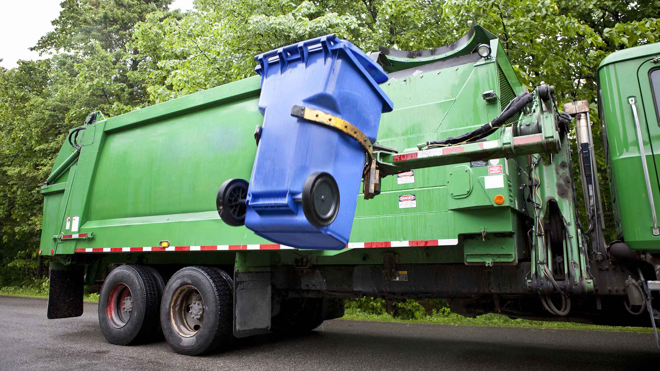 Green garbage truck lifting a blue dumpster