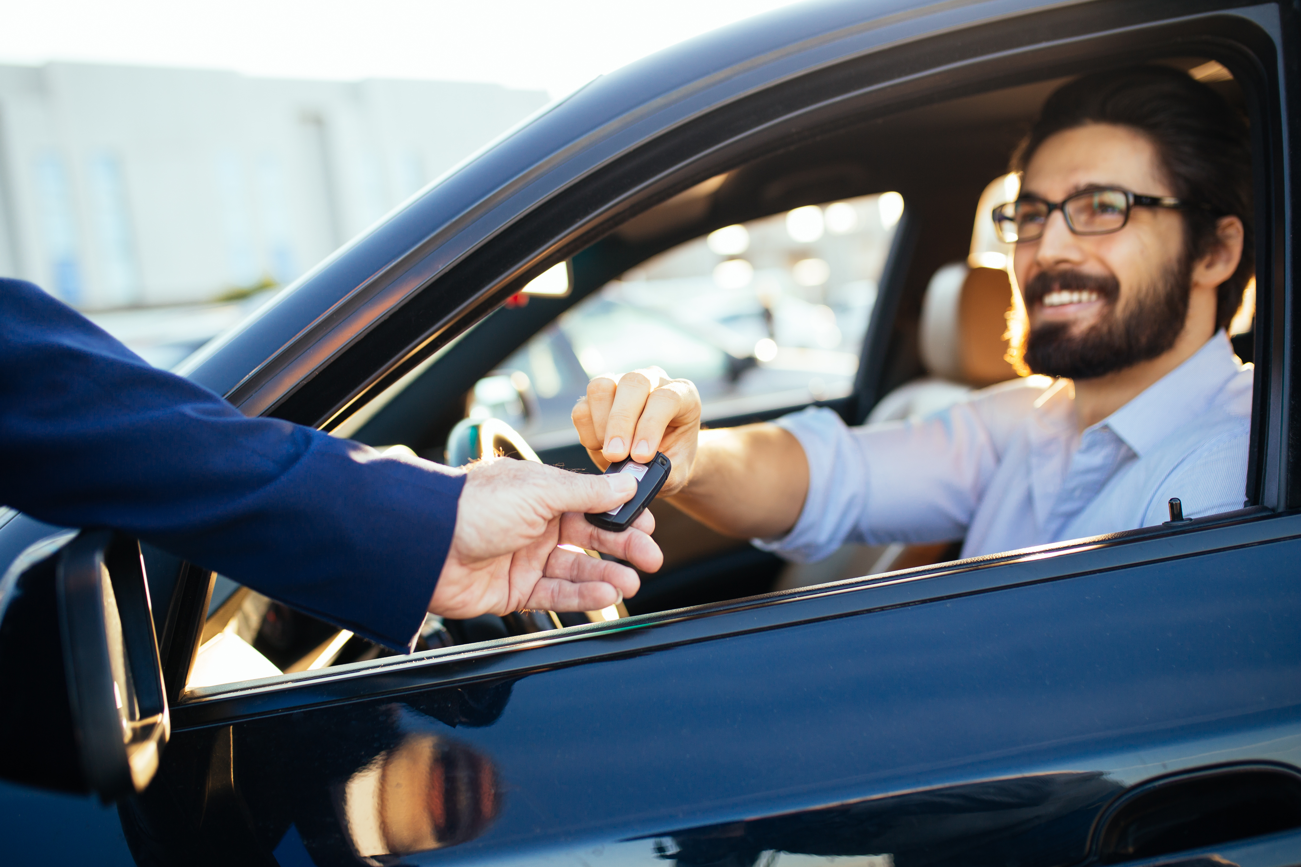 Hombre sonriente dentro de un coche recibiendo las llaves del vehículo a través de la ventanilla