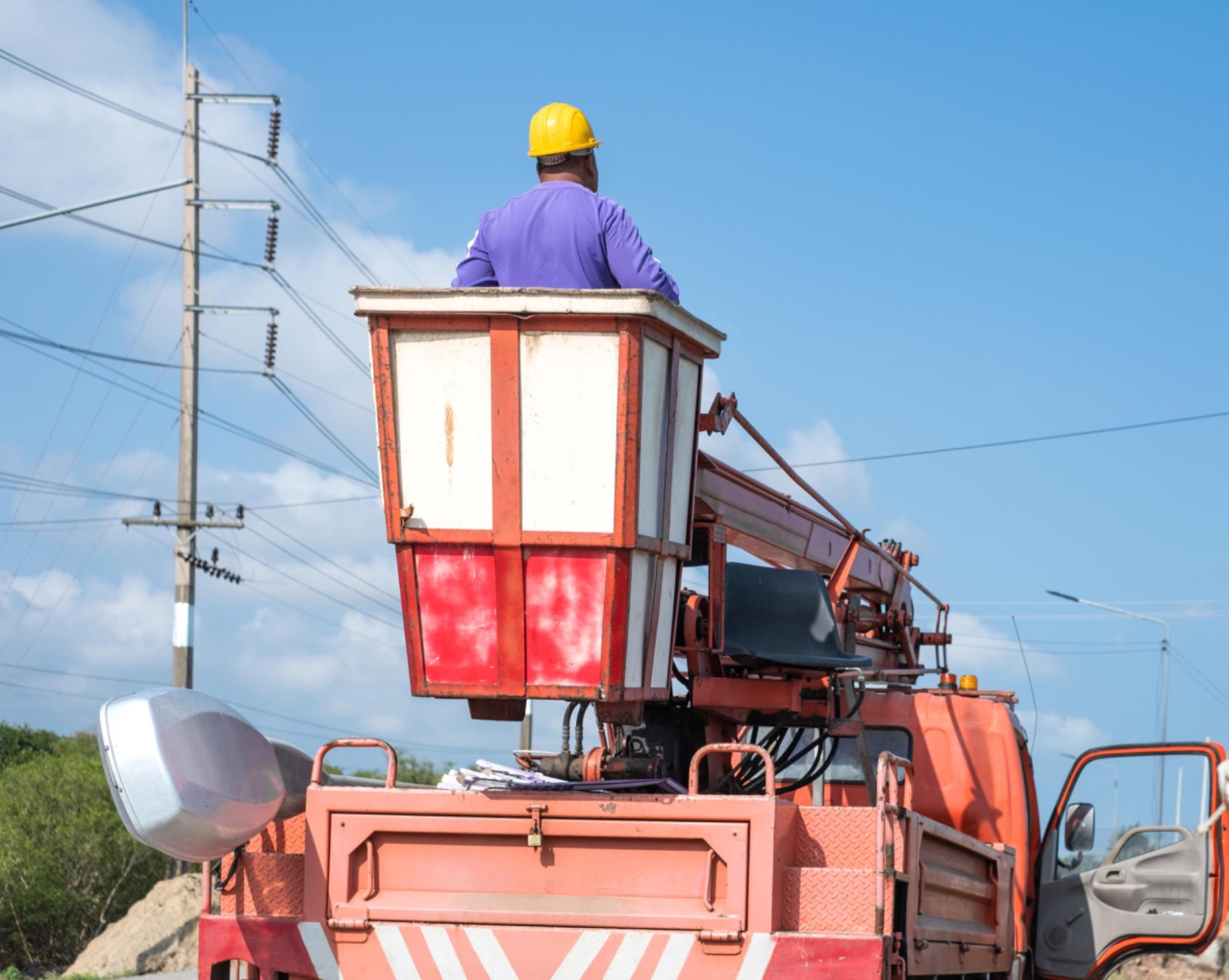 Technicien dans une nacelle de camion-grue à prise de force, intervenant près de lignes électriques.