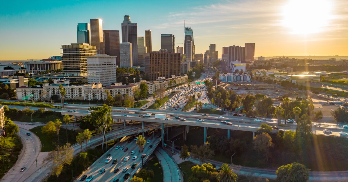 Échangeurs autoroutiers et circulation dense devant les gratte-ciel d'une ville au coucher du soleil.