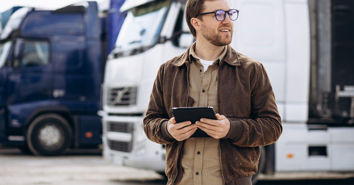 Gestionnaire de flotte utilisant une tablette devant des camions stationnés.
