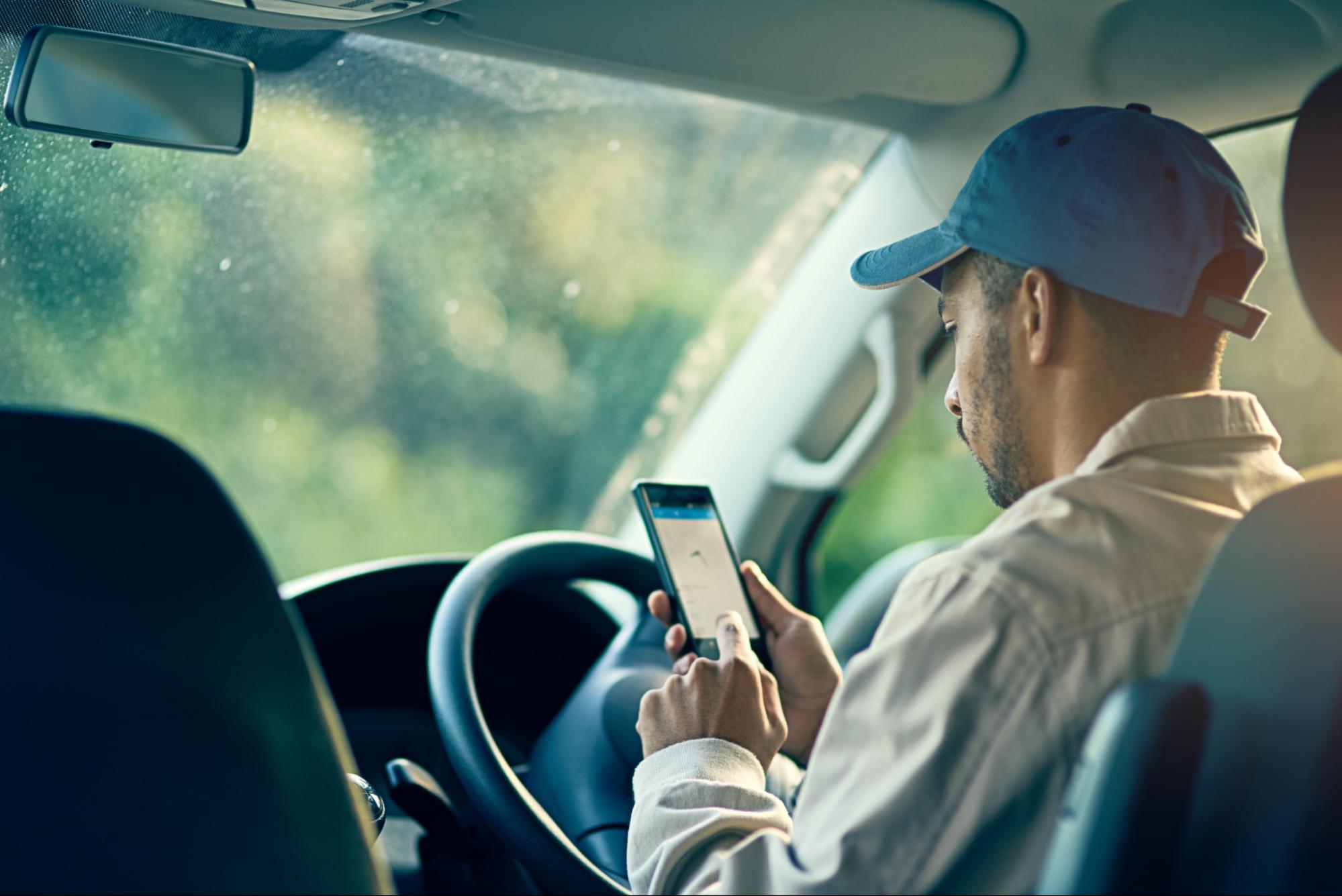 Chauffeur consultant une application sur son smartphone au volant de son véhicule à l'arrêt.
