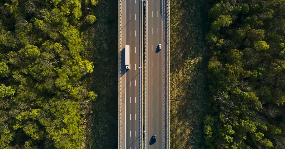 Vue aérienne d'une autoroute rectiligne entre deux forêts, empruntée par un camion.
