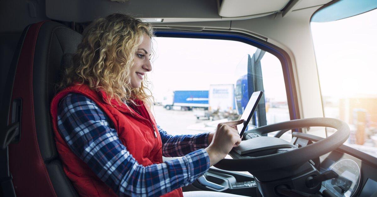Conductrice de camion souriante utilisant une tablette fixée au tableau de bord.