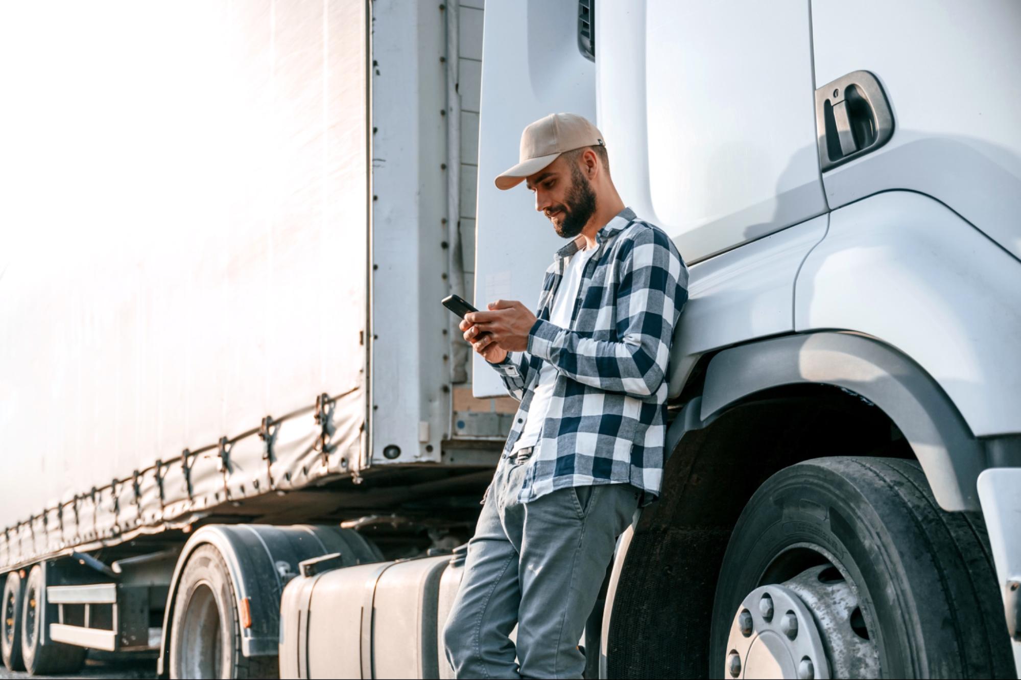 Chauffeur routier adossé à son camion consultant son smartphone.