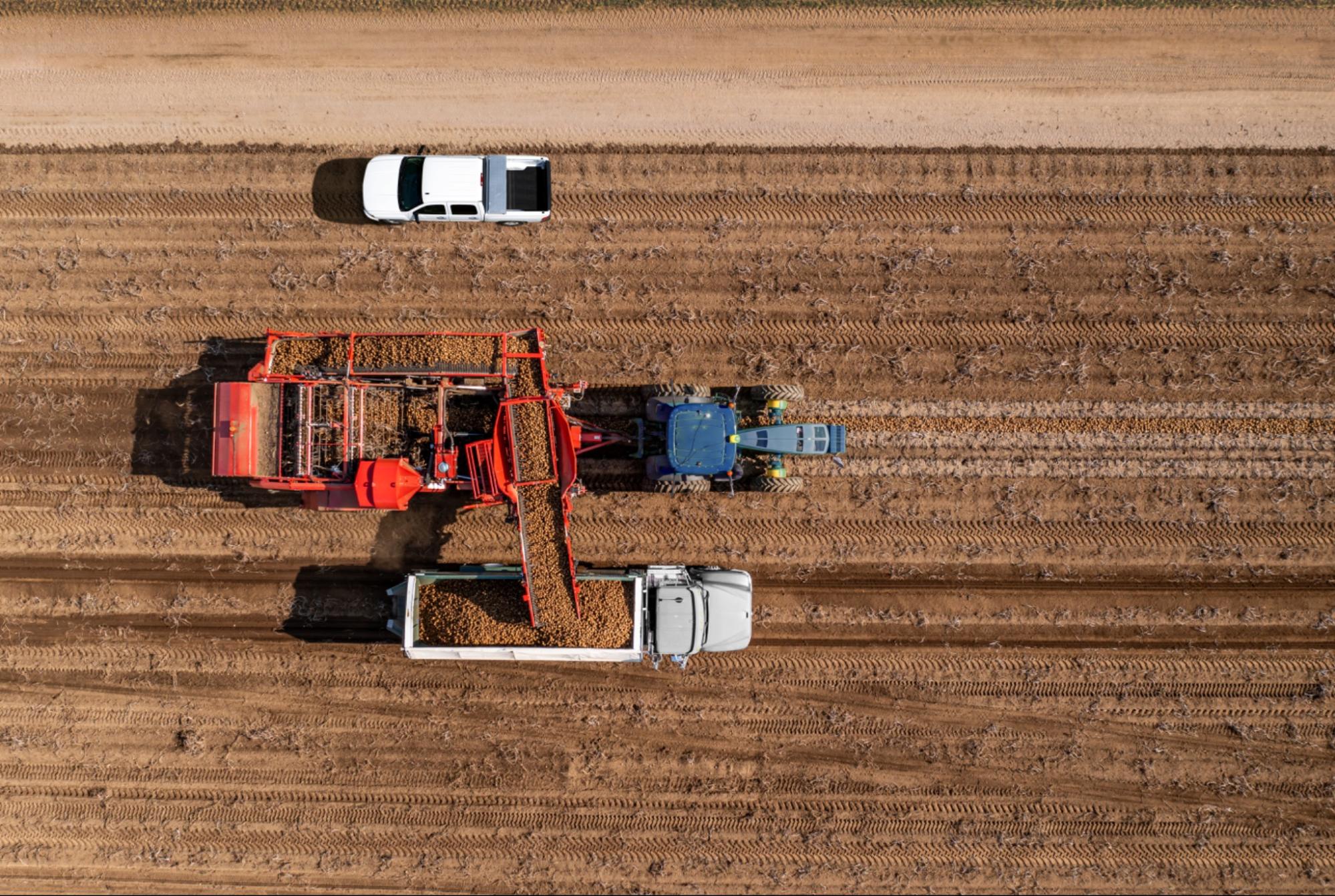 Vue aérienne d'un tracteur entraînant une machine de récolte via la prise de force, déchargeant la récolte dans un camion.