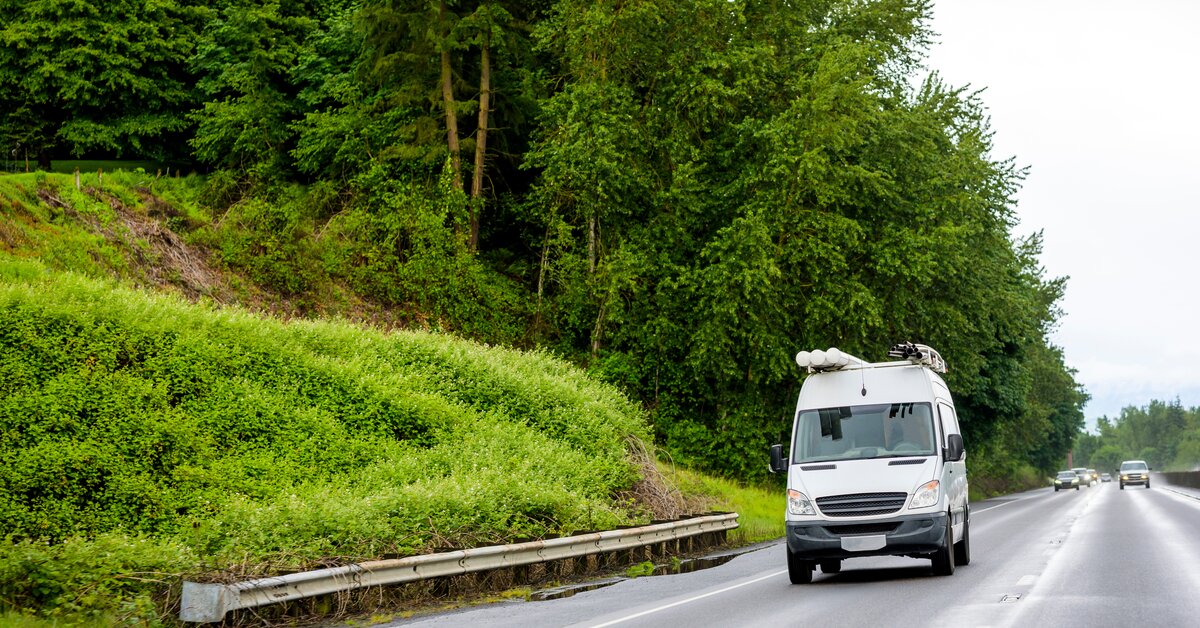 Fourgon utilitaire blanc circulant sur une route bordée de végétation.