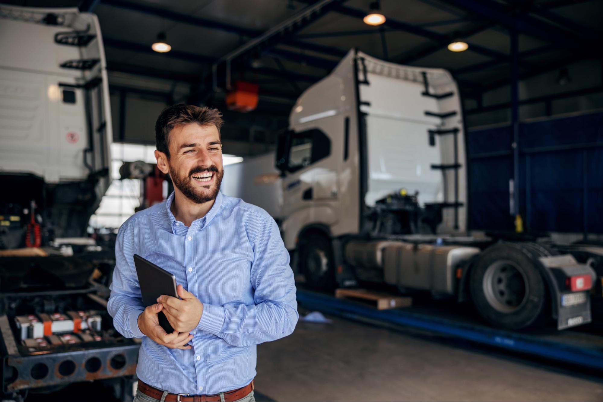 Responsable d'atelier souriant tenant une tablette dans un garage de poids lourds.