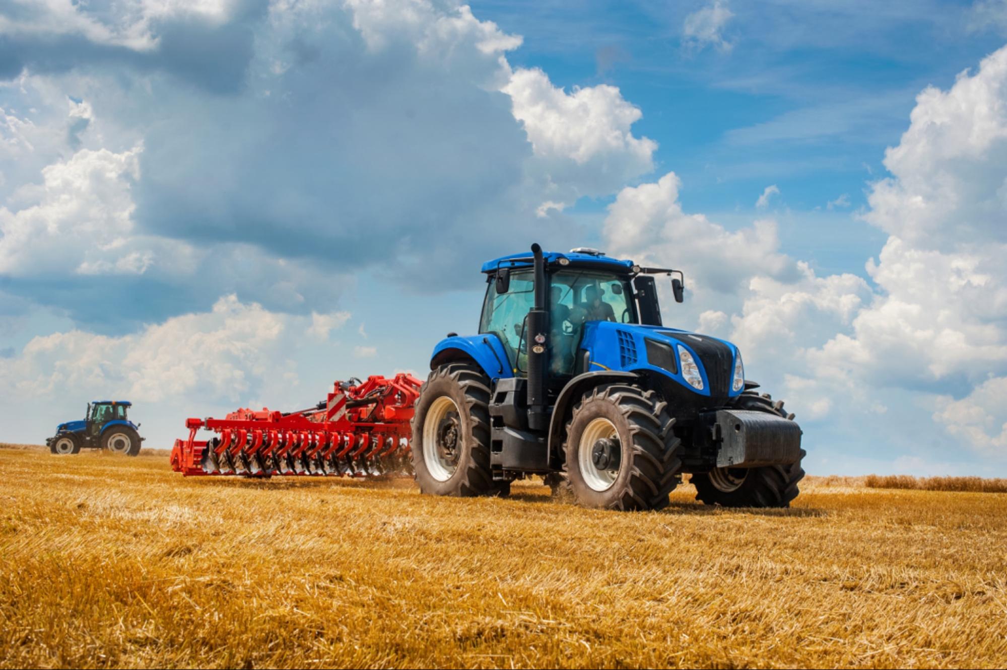 Tracteur bleu tirant un outil agricole à disques entraîné par la prise de force dans un champ moissonné.