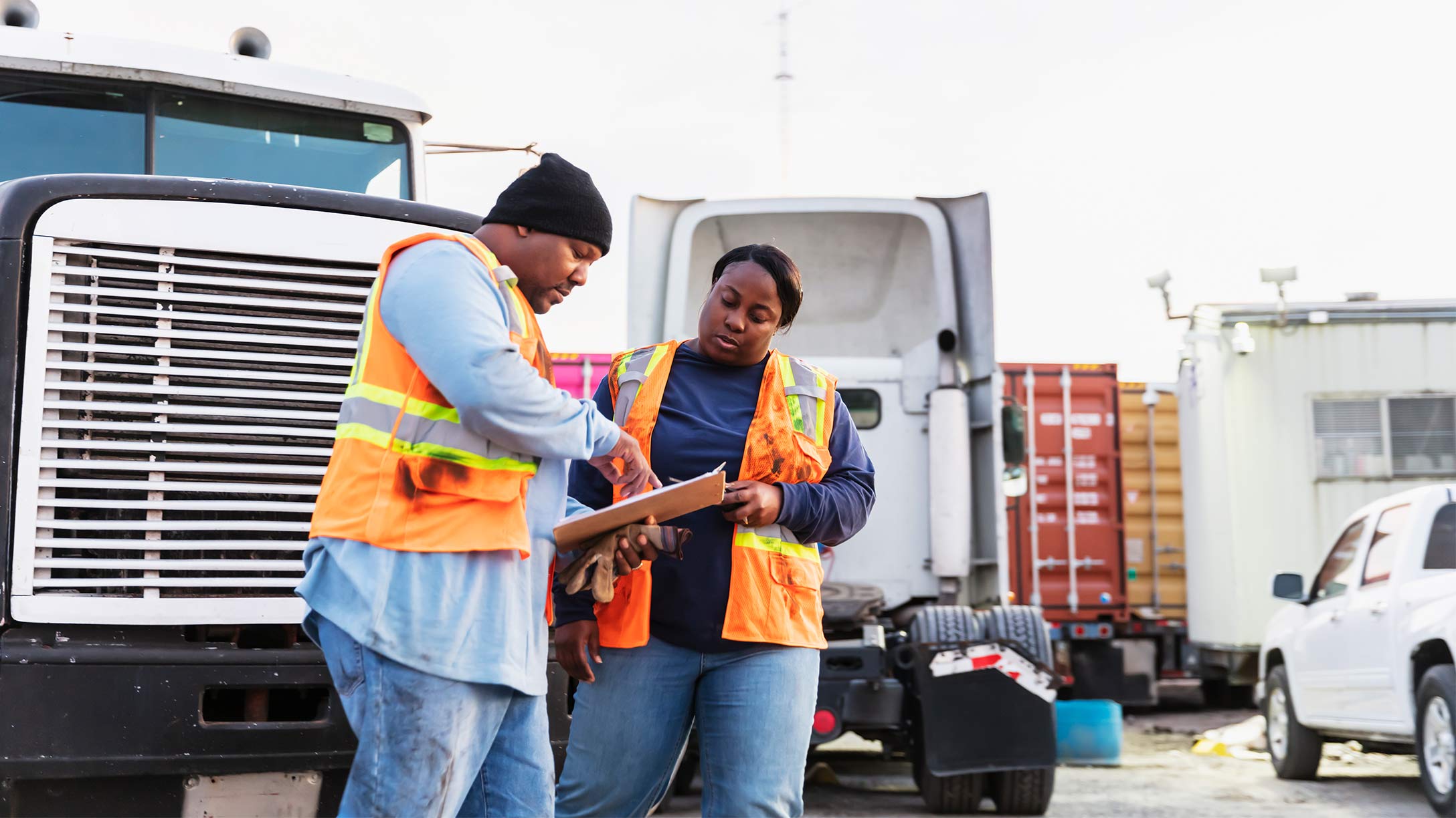 A man and a woman in work wear standing in front of a truck looking at some documents.