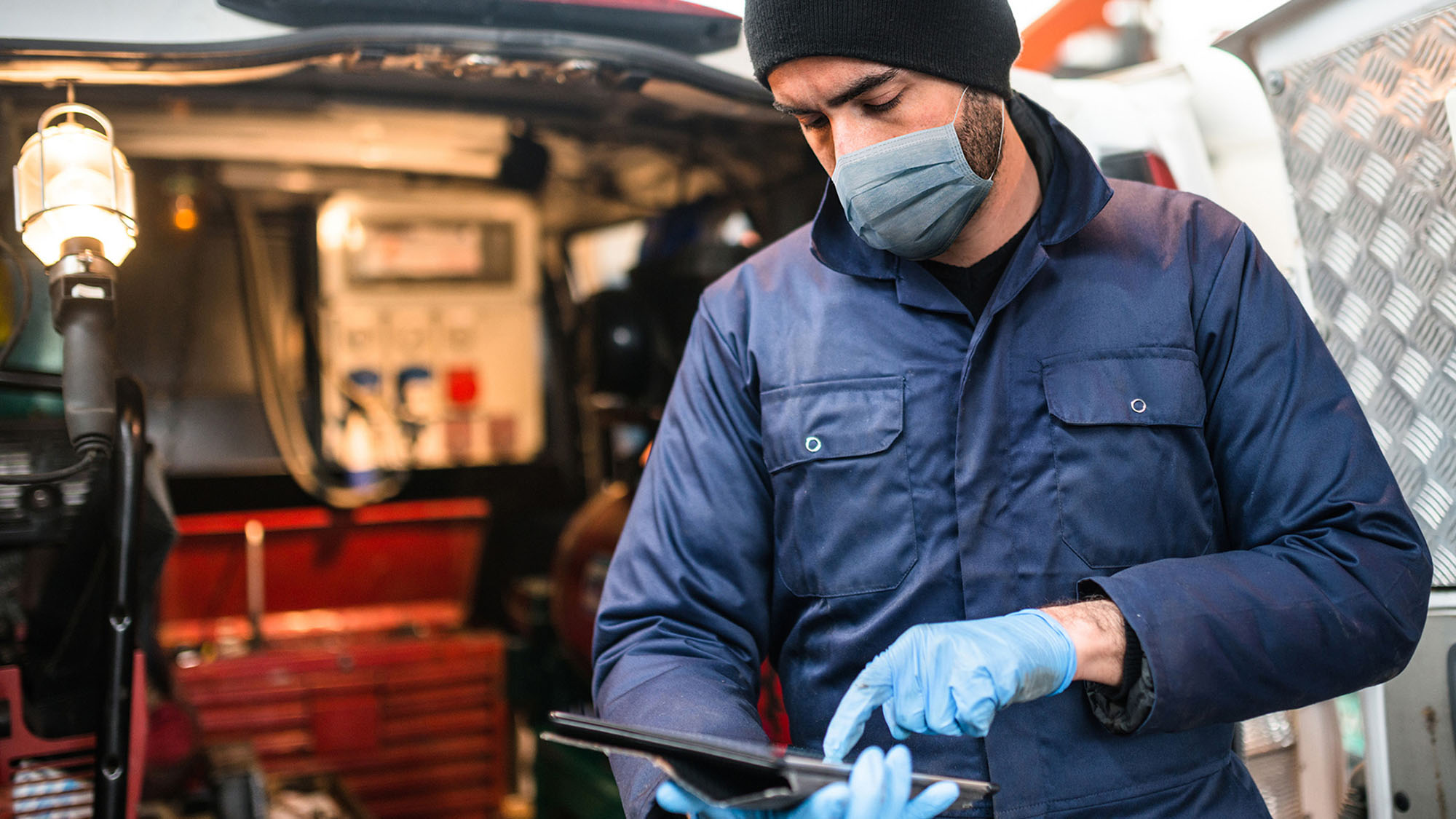 Man wearing mask in front of a truck checking a tablet electronic logging device