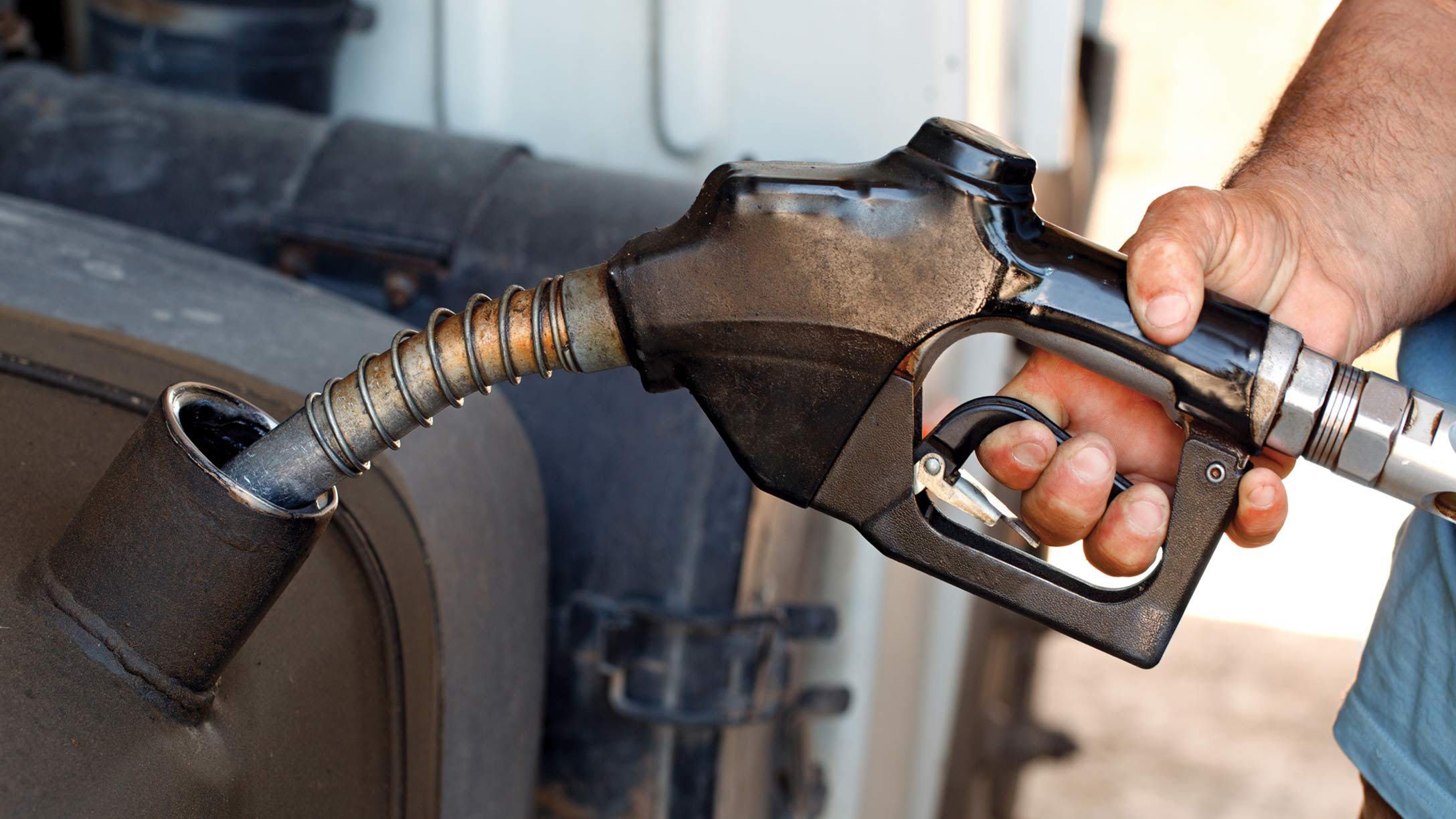A hand holding a fuel nozzle to a vehicle's gas tank