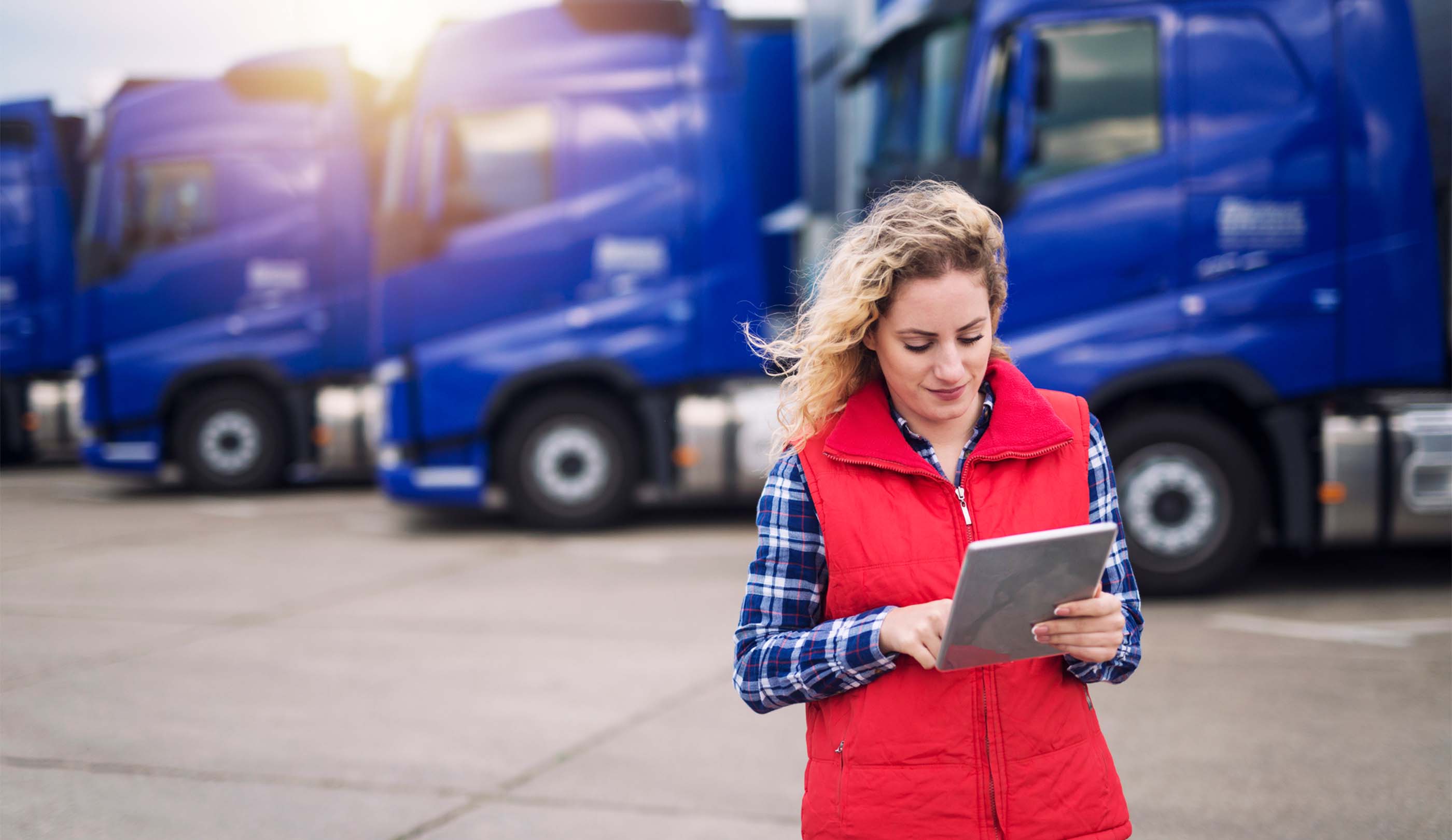 Woman in a red vest in front of blue trucks looking at a tablet reviewing unassigned yard moves