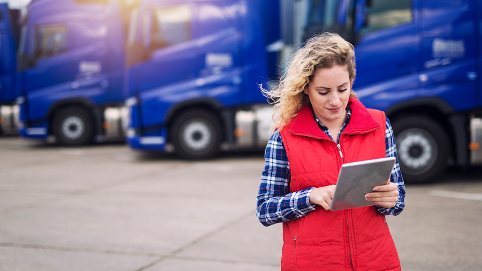 Woman in a red vest in front of blue trucks looking at a tablet reviewing unassigned yard moves