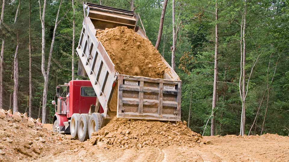 Dump truck dumping soil near a forest